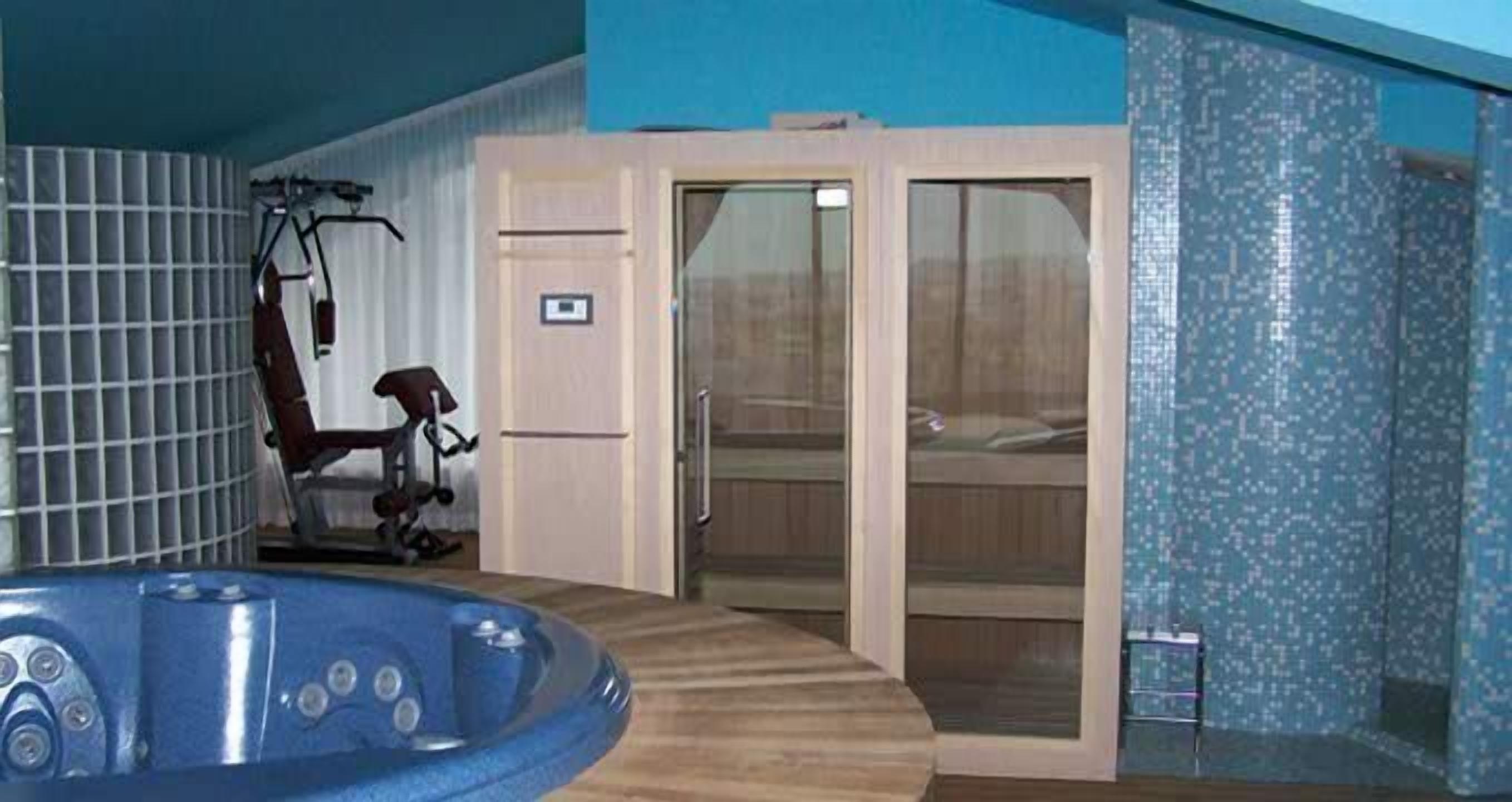 Un cuarto de spa con bañera de hidromasaje, equipo de ejercicio y una puerta corrediza de vidrio que da a una zona de ducha.