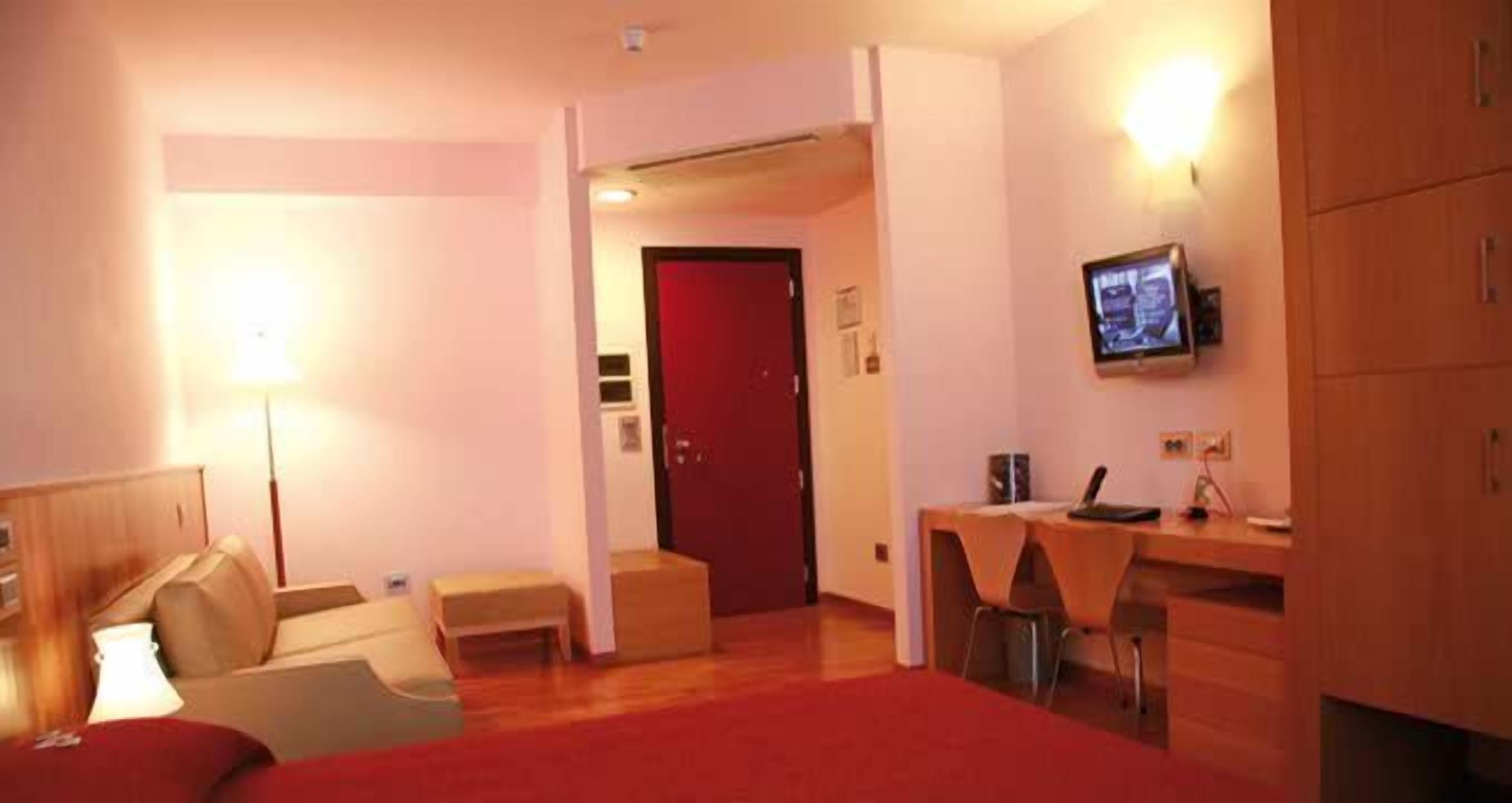 Habitación de hotel con cama, escritorio, silla, televisor y una puerta roja.