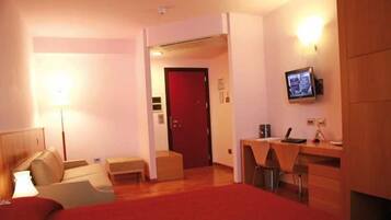 Habitación de hotel con cama, escritorio, silla, televisor y una puerta roja.