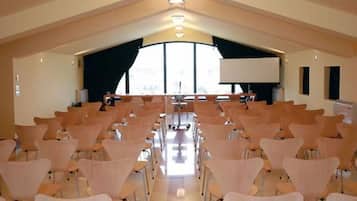 Una sala conferenze con file di sedie rivolte verso uno schermo grande, un podio e una finestra che lascia entrare luce naturale.
