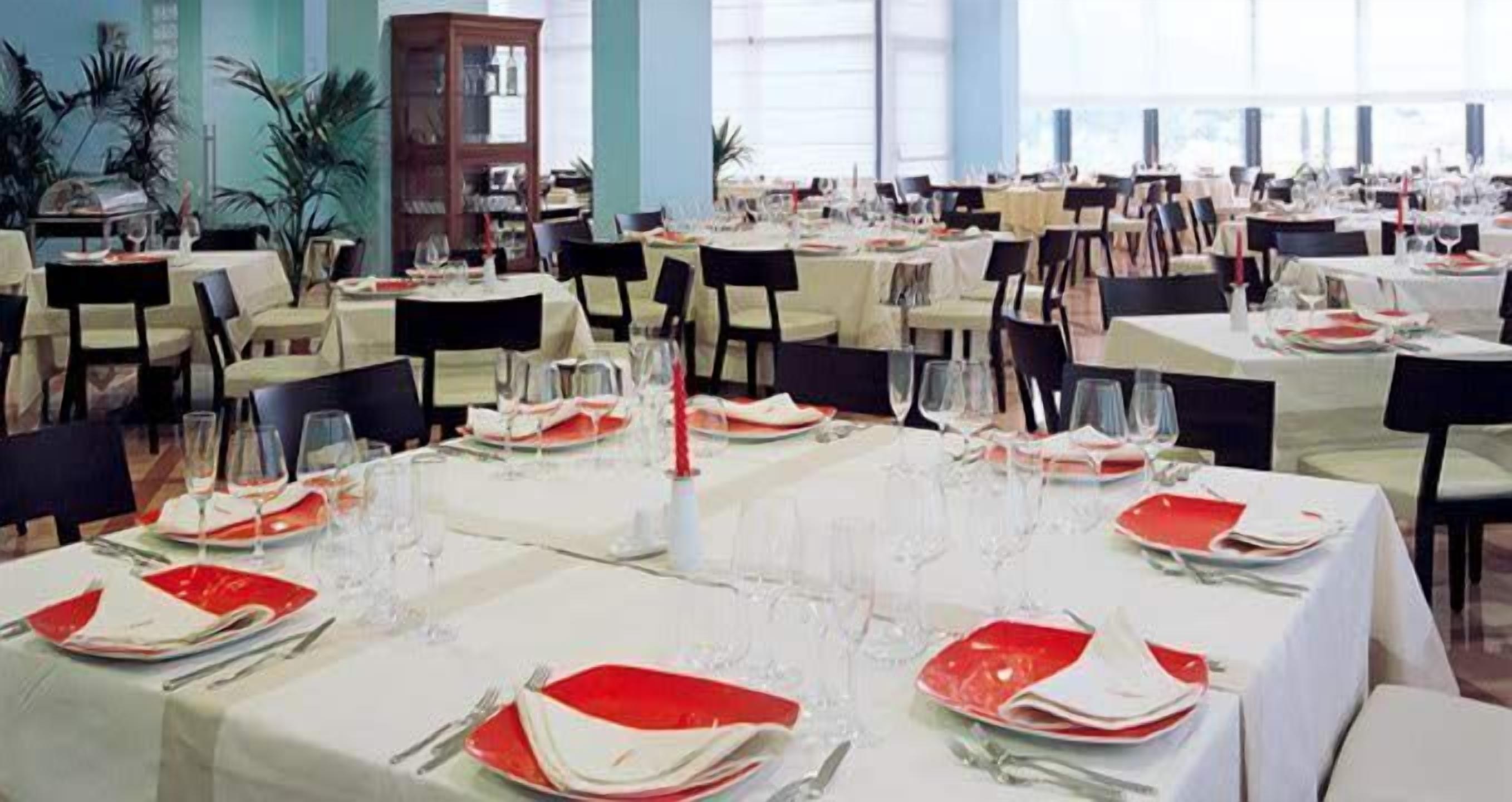 A formal dining area with tables set for multiple guests, featuring white tablecloths and red plates.