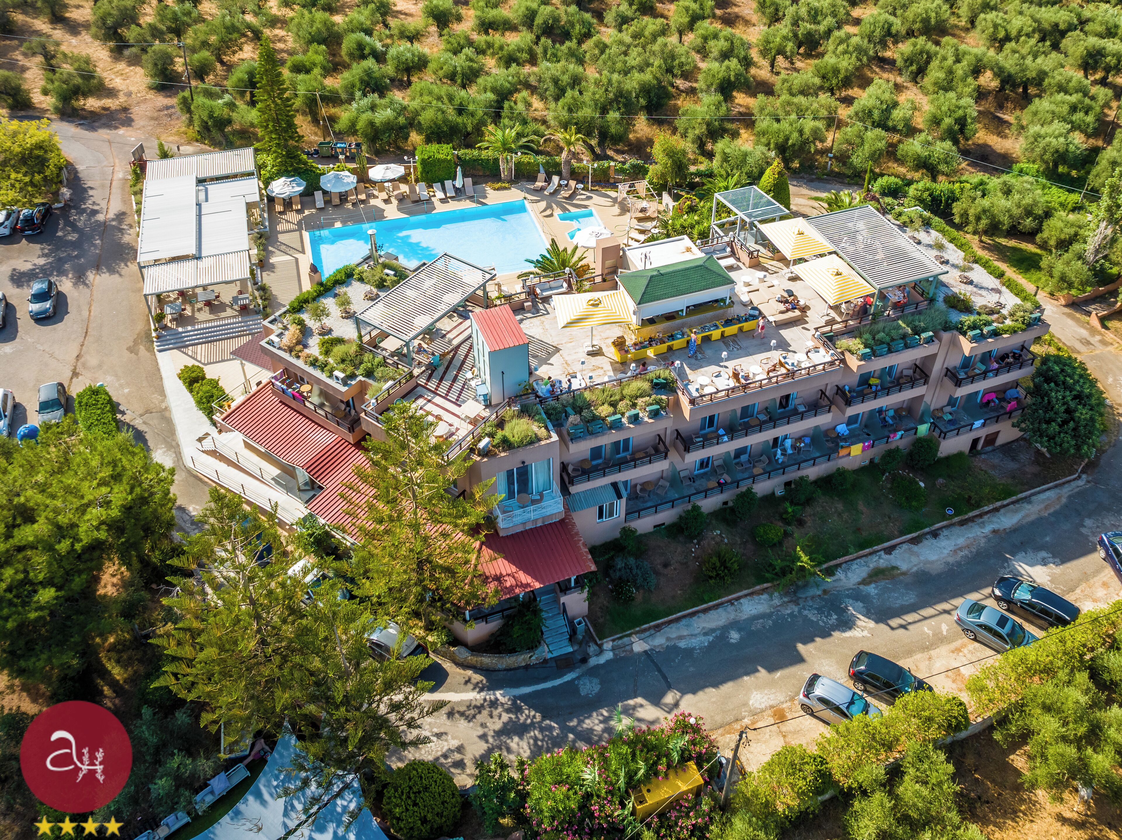 An aerial view of a hotel with a swimming pool, outdoor seating, and a rooftop garden.