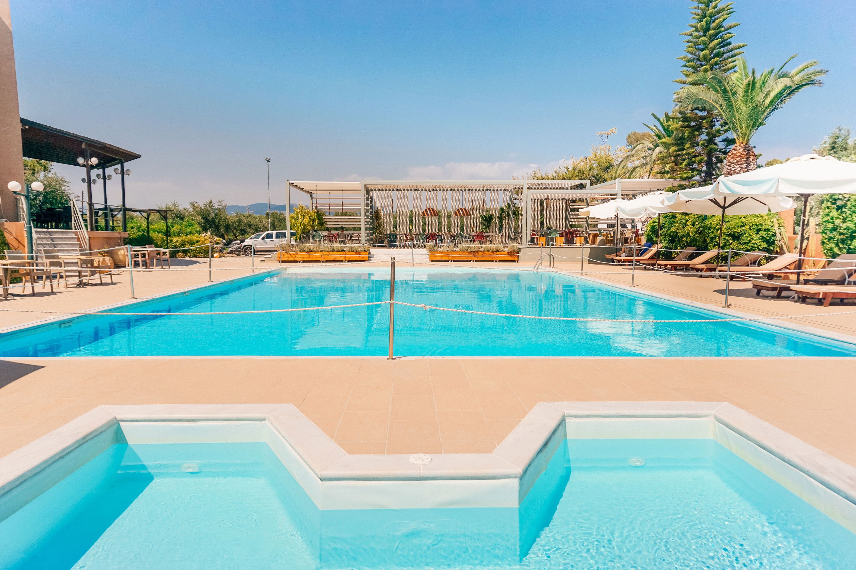 A swimming pool with lounge chairs and umbrellas, surrounded by palm trees and a covered seating area.