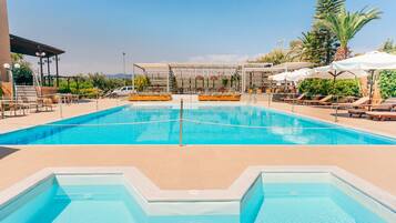 Une piscine entourée de palmiers, avec des chaises longues et des parasols, ainsi qu’un espace de détente abrité.