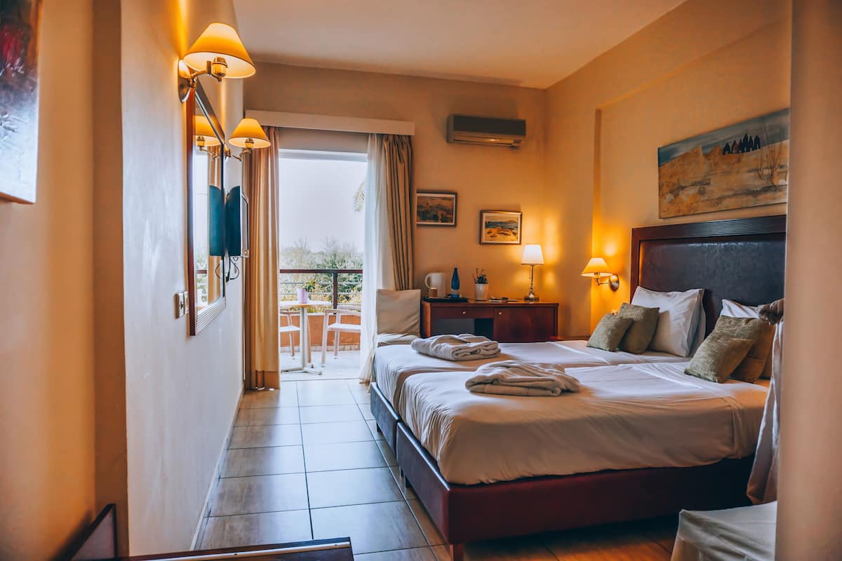 A hotel room with a large bed, two bedside tables, a desk, a chair, a balcony, and a painting on the wall.