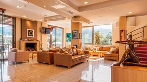 A spacious living room with a fireplace, comfortable seating, and large windows offering a view of the outdoors. - Apollo Resort Art Hotel (Trifylia)