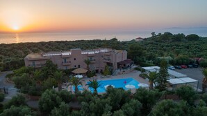 A resort with a swimming pool, multiple buildings, and a view of the sea at sunset. - Apollo Resort Art Hotel (Trifylia)