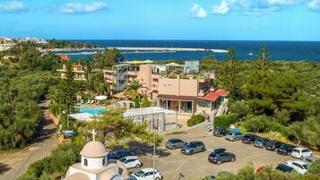 A coastal hotel with a swimming pool, parking area, and a view of the sea.