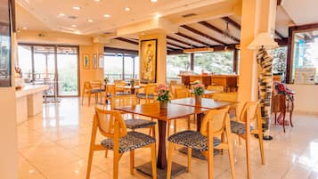 Un vaste espace dédié à la salle à manger, avec des tables et des chaises en bois, de grandes fenêtres et une vue sur l’extérieur.