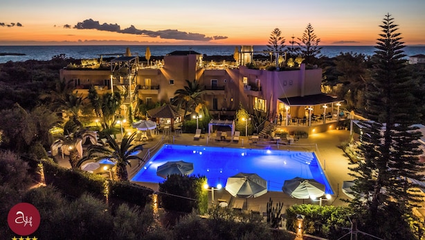 A resort with a swimming pool, outdoor seating, and a view of the ocean at sunset. - Apollo Resort Art Hotel (Trifylia)
