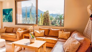 A modern living room with a large window, leather sofas, a wooden coffee table, and a cactus plant. - Apollo Resort Art Hotel (Trifylia)