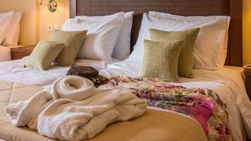 A hotel room with a large bed, a headboard, a painting above the bed, a nightstand with a lamp, and a wall-mounted air conditioner.