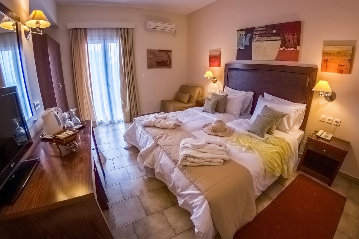 A hotel room with a large bed, bedside lamps, a desk with a telephone, and a TV.