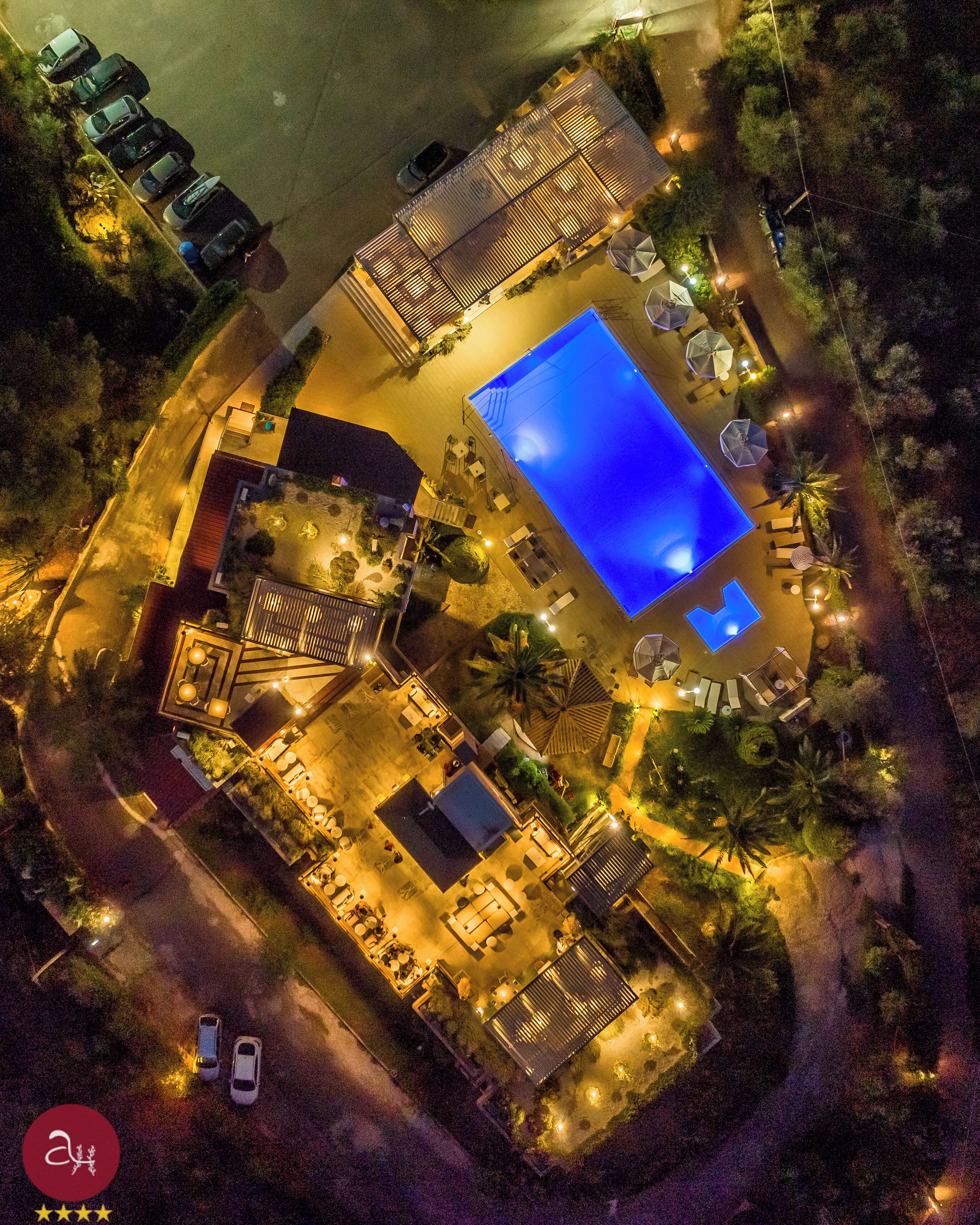 Vue aérienne d’un complexe hôtelier doté d’une piscine, d’un espace extérieur aménagé avec des sièges et d’une terrasse bien éclairée.