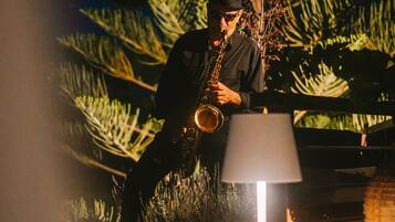 En person spiller saxofon udendørs om natten, med en lampe og noget vegetation i baggrunden.