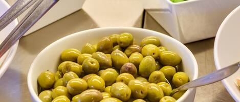 A bowl of olives with a spoon, surrounded by salad containers.