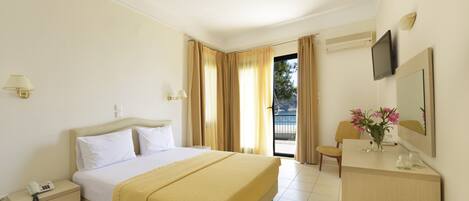 A hotel room with a bed, bedside table, lamp, and a desk with a mirror and flowers.