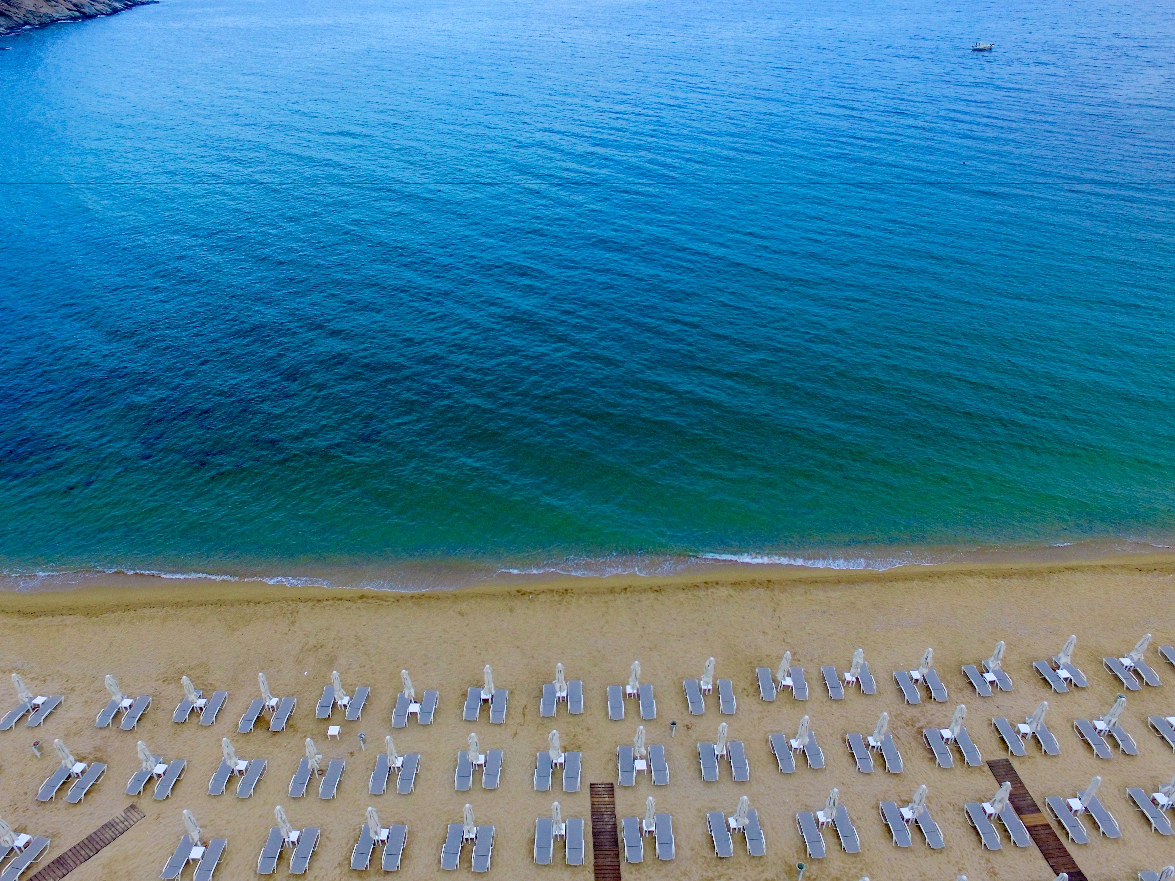 Eine Luftaufnahme eines Strandes mit Reihen von Liegestühlen und Sonnenschirmen, einem sandigen Ufer und ruhigem Meer.