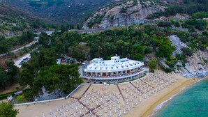 Vista aérea de un hotel costero con zona de playa que incluye filas de tumbonas y una piscina.