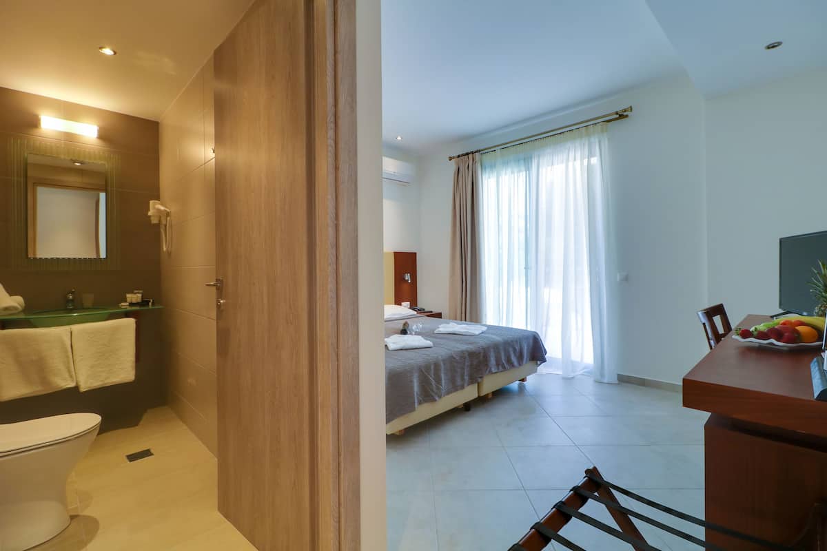 A hotel room with a bathroom, a bed with a large window, and a dining area with fruit.