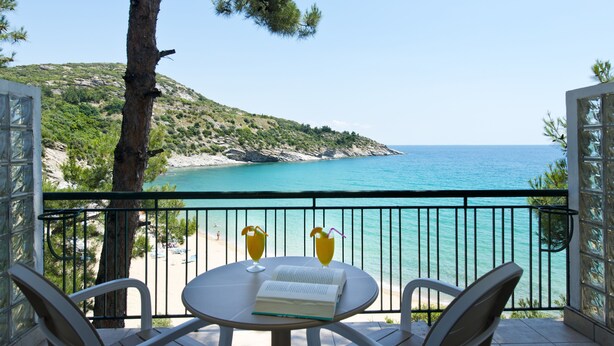Un balcón con una mesa, dos sillas y dos bebidas. El balcón tiene vistas a la playa y al mar.
