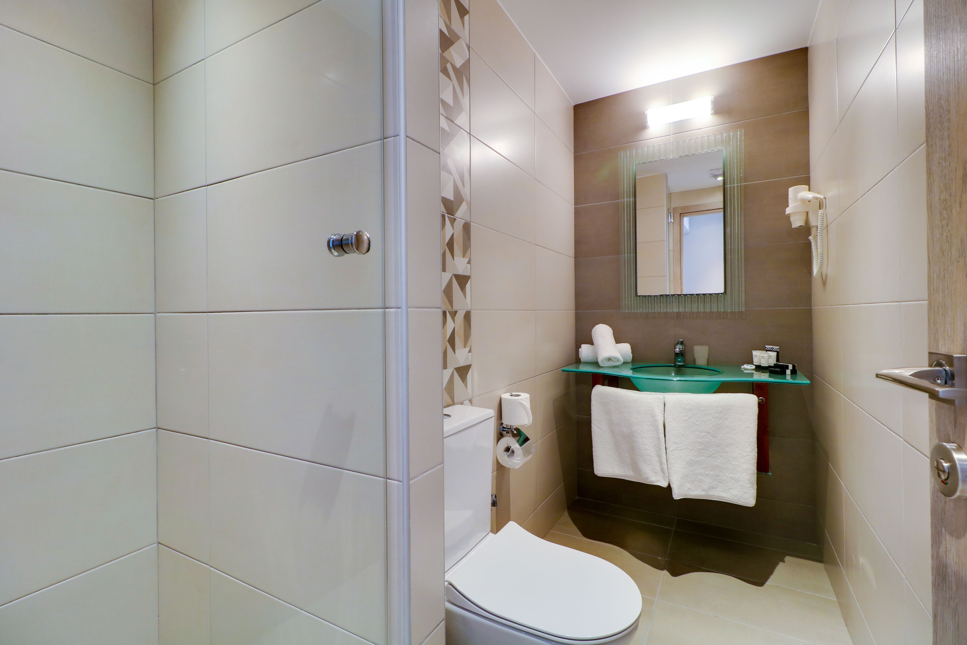 A bathroom with a toilet, sink, and mirror. There are towels hanging on the wall and a shower area.