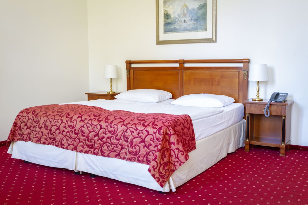 A hotel room with a large bed, two bedside tables, a nightstand, and a painting on the wall.