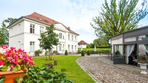 Ein großes weißes Gebäude mit rotem Dach, einem gepflasterten Innenhof und einer kleinen Außenbestuhlung.