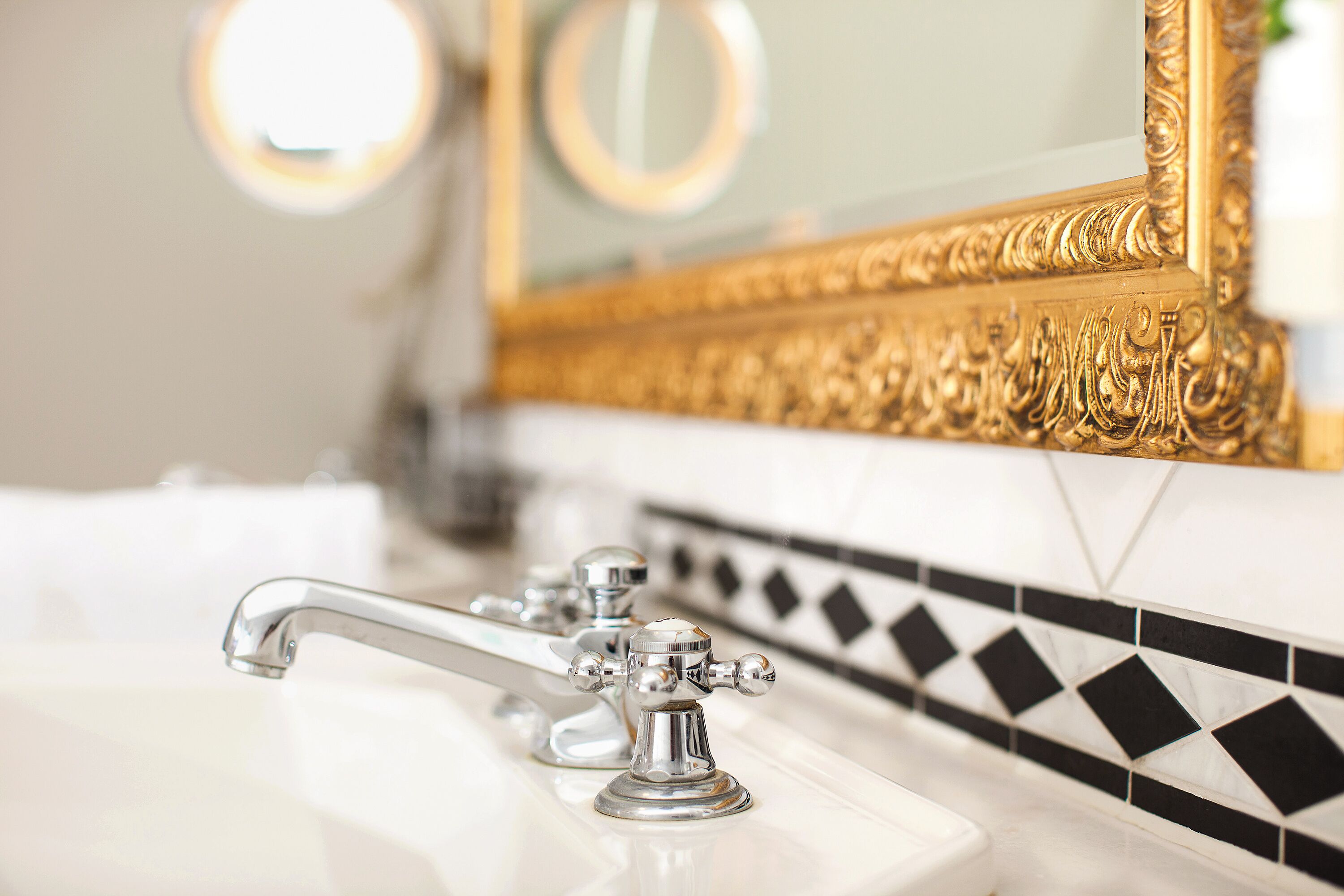 A bathroom with a white sink, chrome faucets, and a gold-framed mirror.
