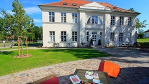 Ein großes, weißes Gebäude mit rotem Dach, einem gepflasterten Innenhof und Außenplätzen mit einem Tisch, der für eine Mahlzeit gedeckt ist.