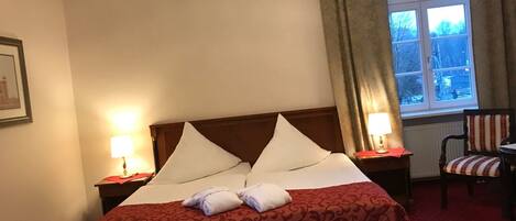 Habitación de hotel con cama, dos lámparas de noche, una silla y ventana con cortinas.