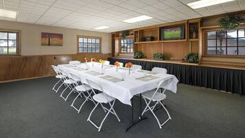 A conference room with a long table set for meetings, white folding chairs, and a television on a wooden shelf.