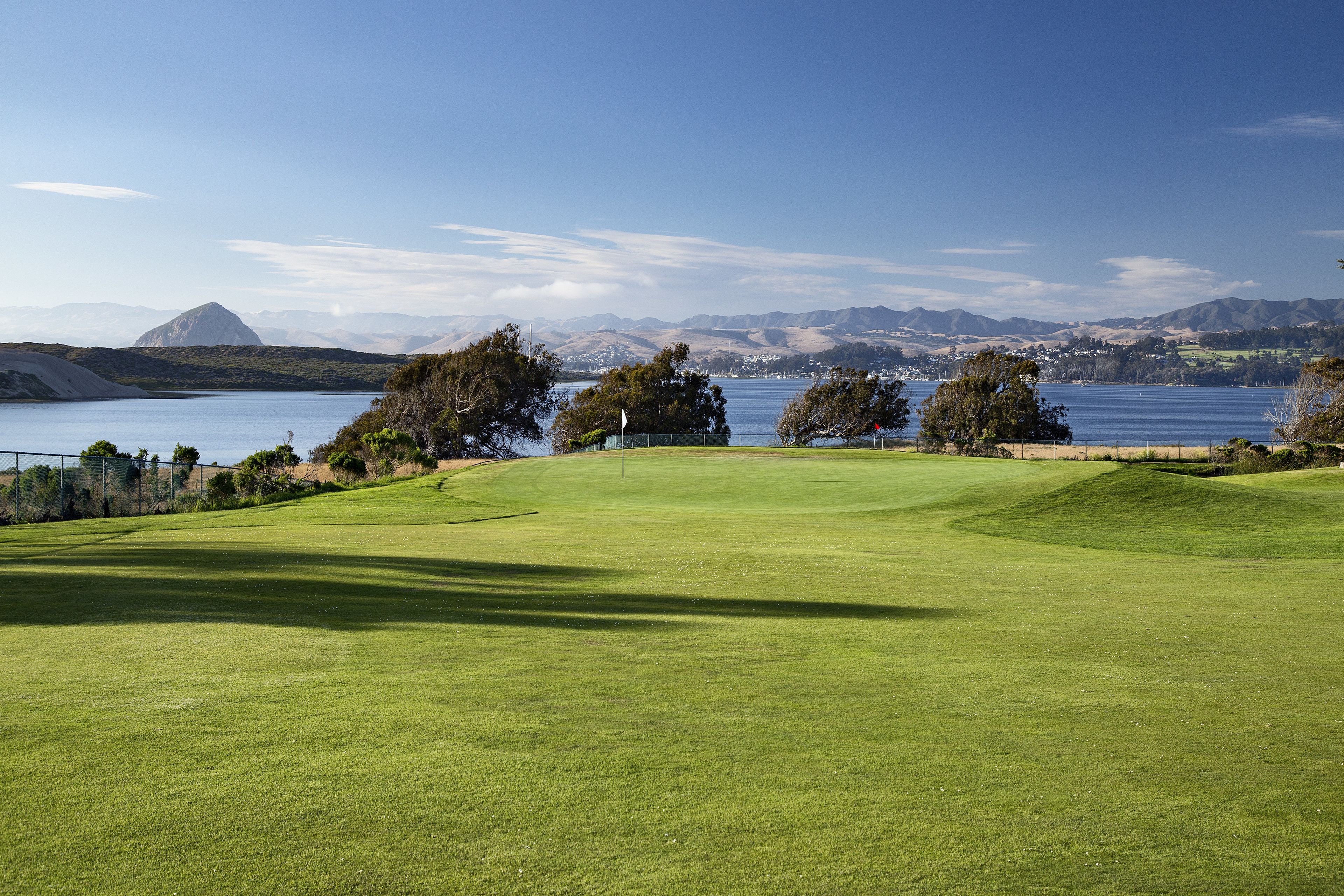 A golf course with a clear view of a lake and mountains in the background.