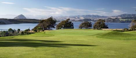 A golf course with a clear view of a lake and mountains in the background.