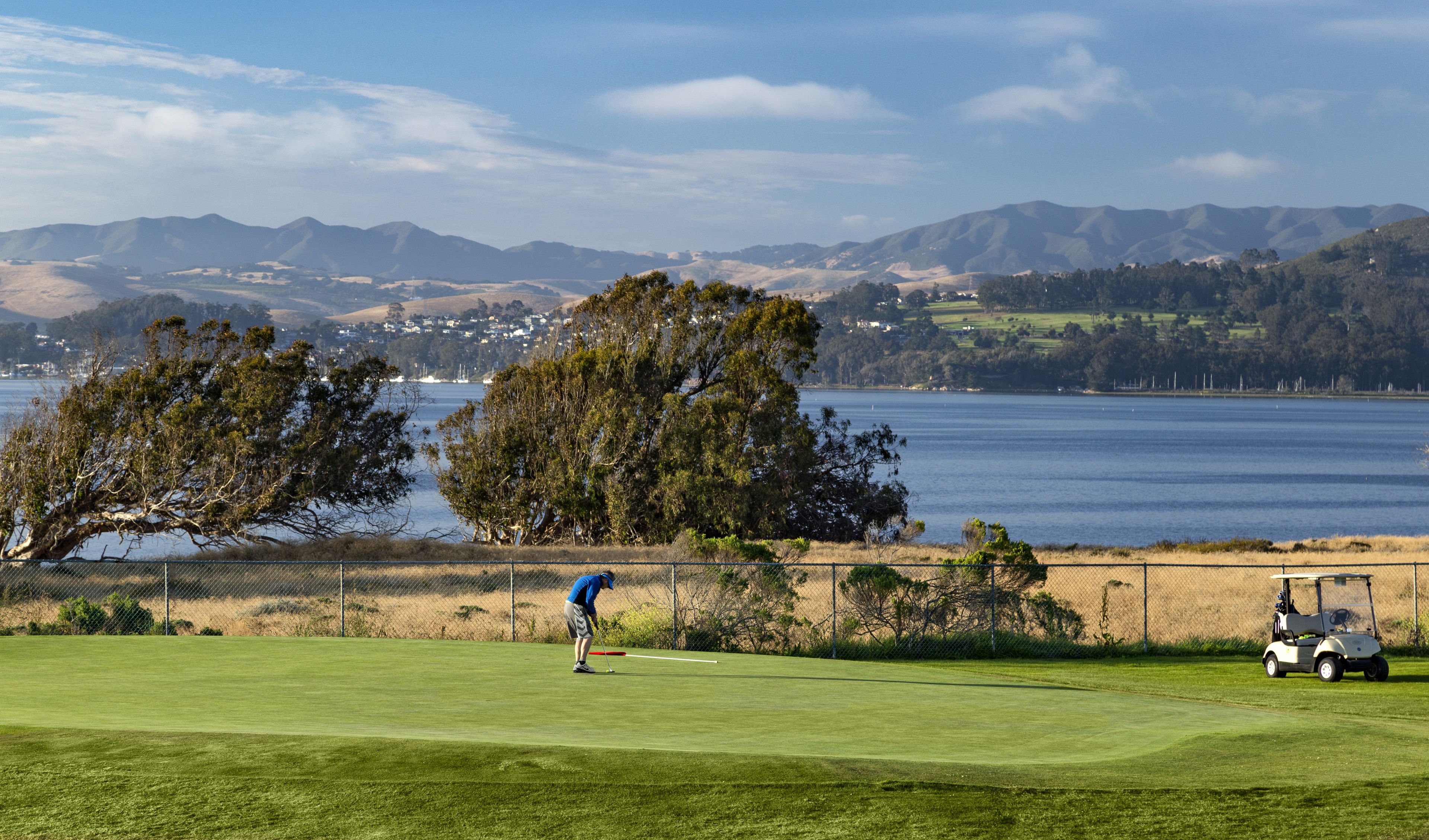 Campo de golf con vistas a un lago y montañas al fondo.