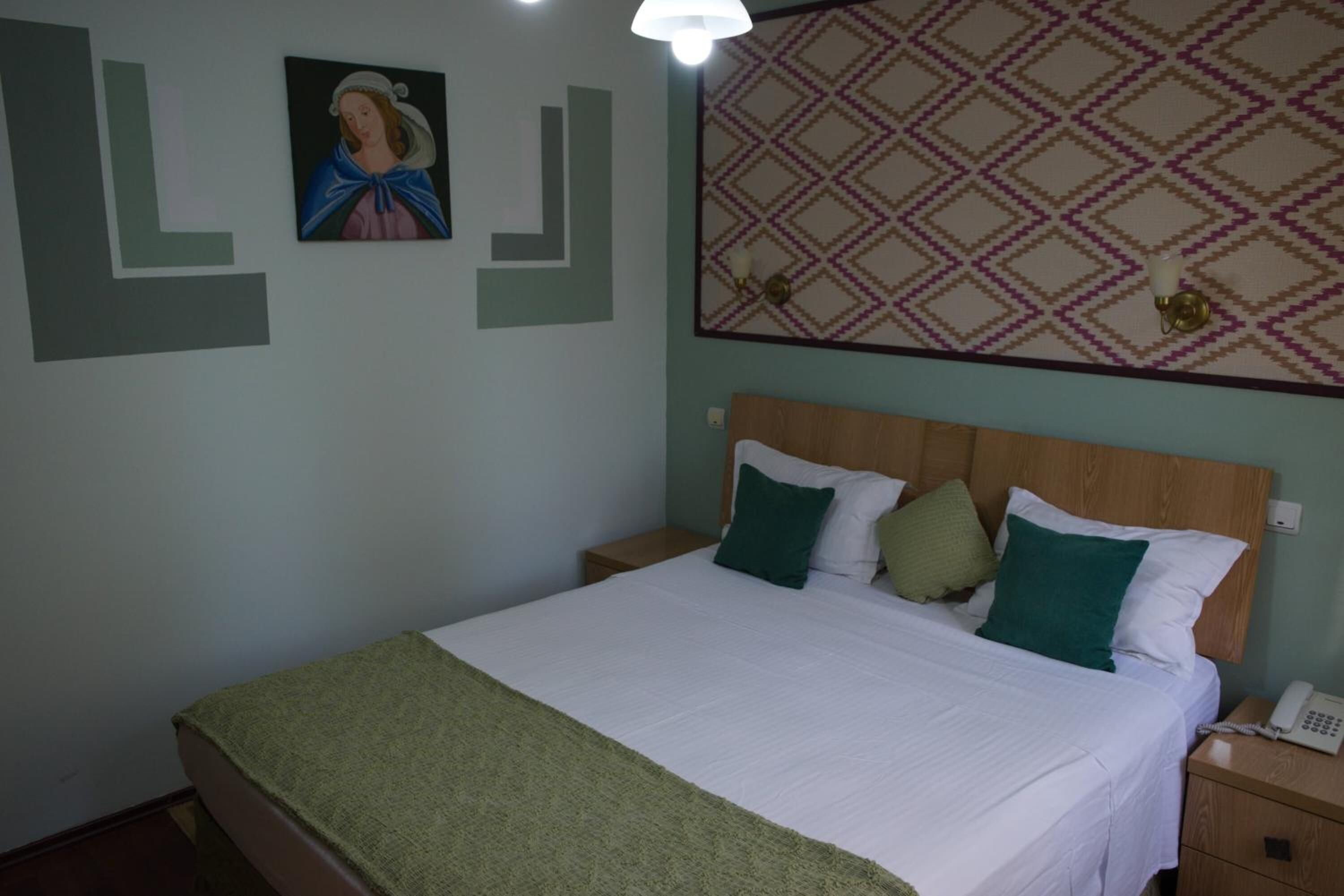 A neatly made bed with a green blanket, a wooden headboard, and two bedside tables with lamps.