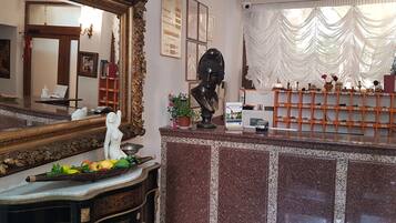 A reception area with a marble counter, a large ornate mirror, a bust sculpture, and a display of trophies.