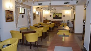 A dining area with yellow chairs and tables, chandeliers, and framed artwork on the walls.