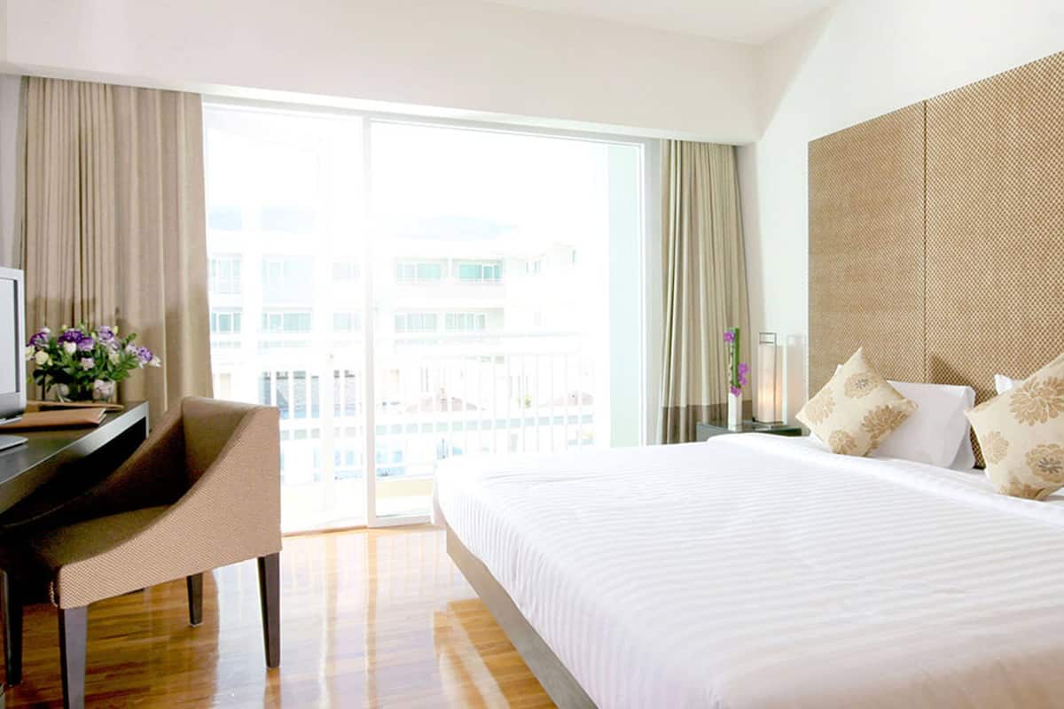 Een hotelkamer met een bed, een bureau met een computer en uitzicht op buiten.