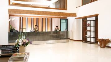 A hotel reception area with a modern design, featuring a reception desk, a guest relation sign, and a decorative vase with flowers.