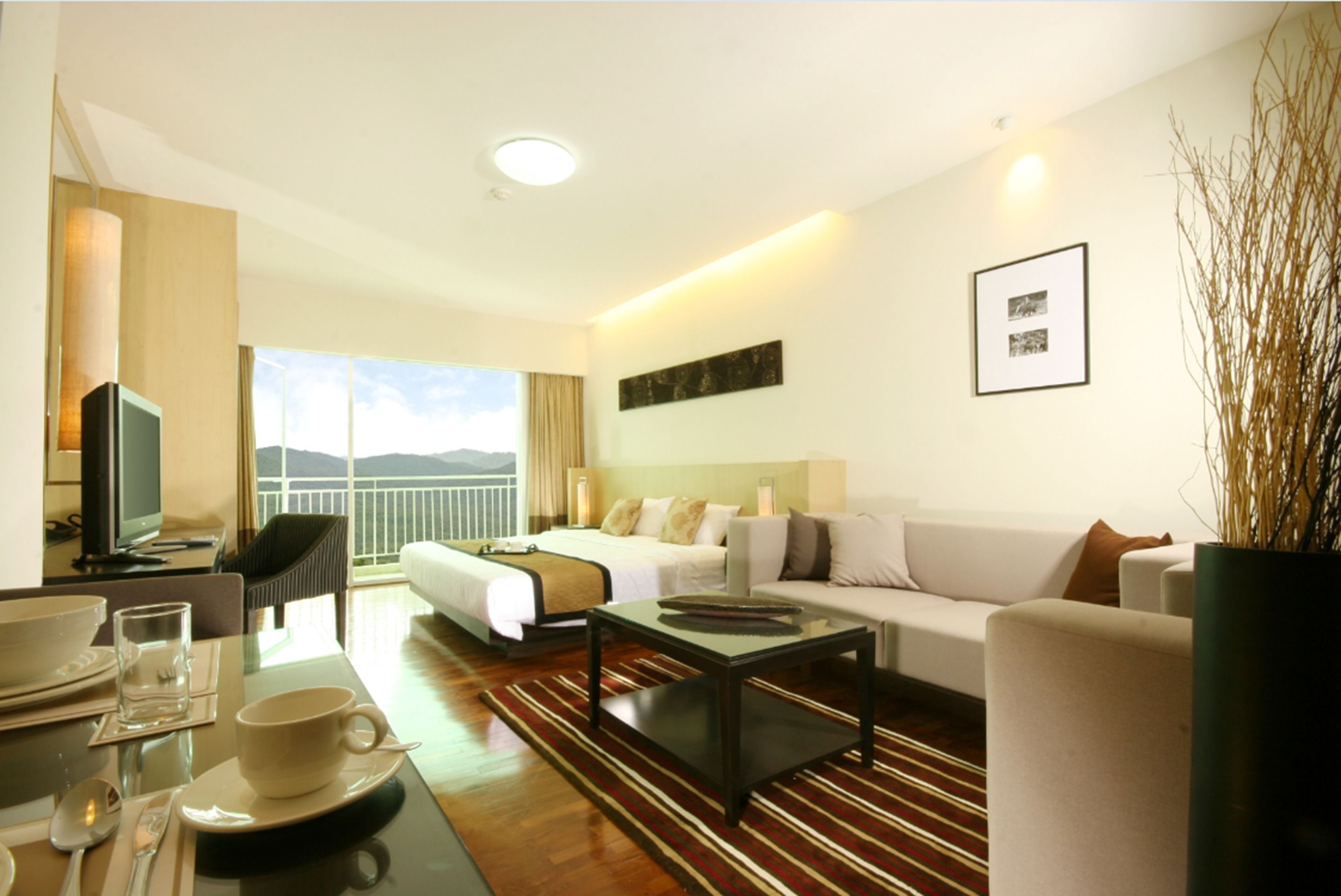 A hotel room with a bed, a sofa, a coffee table, a TV, and a dining area with a table set for two.