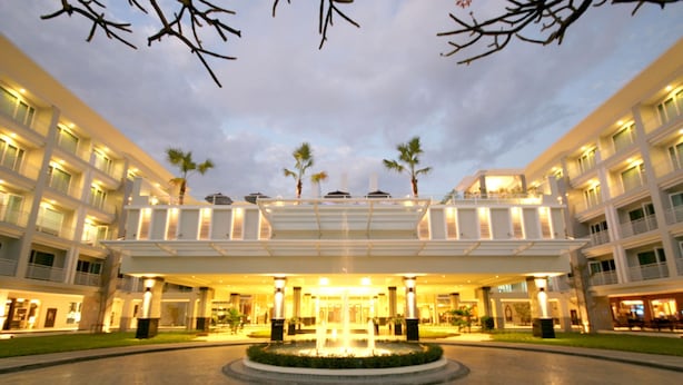 A hotel entrance with a central fountain, multiple floors, and palm trees.