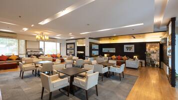 A spacious hotel lobby with multiple seating areas, including sofas and tables, and a large television screen.