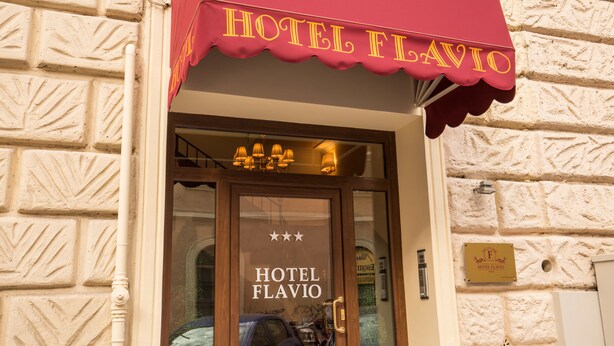 The entrance of Hotel Flavio with a red awning and a glass door displaying the hotel's name. - Hotel Flavio Rome (Rome)