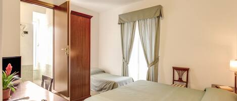 Habitación de hotel con una cama, un escritorio con teléfono y una planta, una silla y un armario.