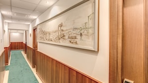A hallway with a green carpet, wooden paneling, and a large framed artwork on the wall. - Hotel Flavio Rome (Rome)