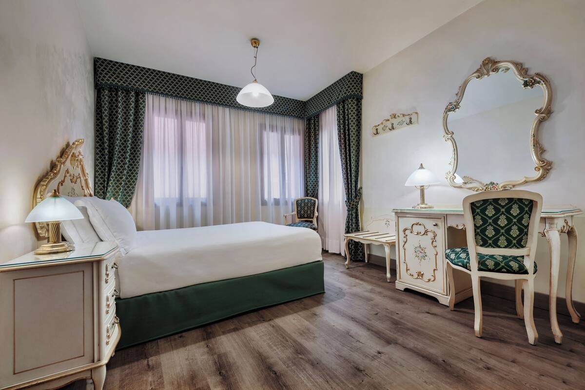 Een hotelkamer met een bed, bureau, stoel, spiegel en raam met gordijnen.