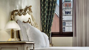 A hotel room with a bed, a nightstand with a lamp, and a view of a building with a clock tower through the window.