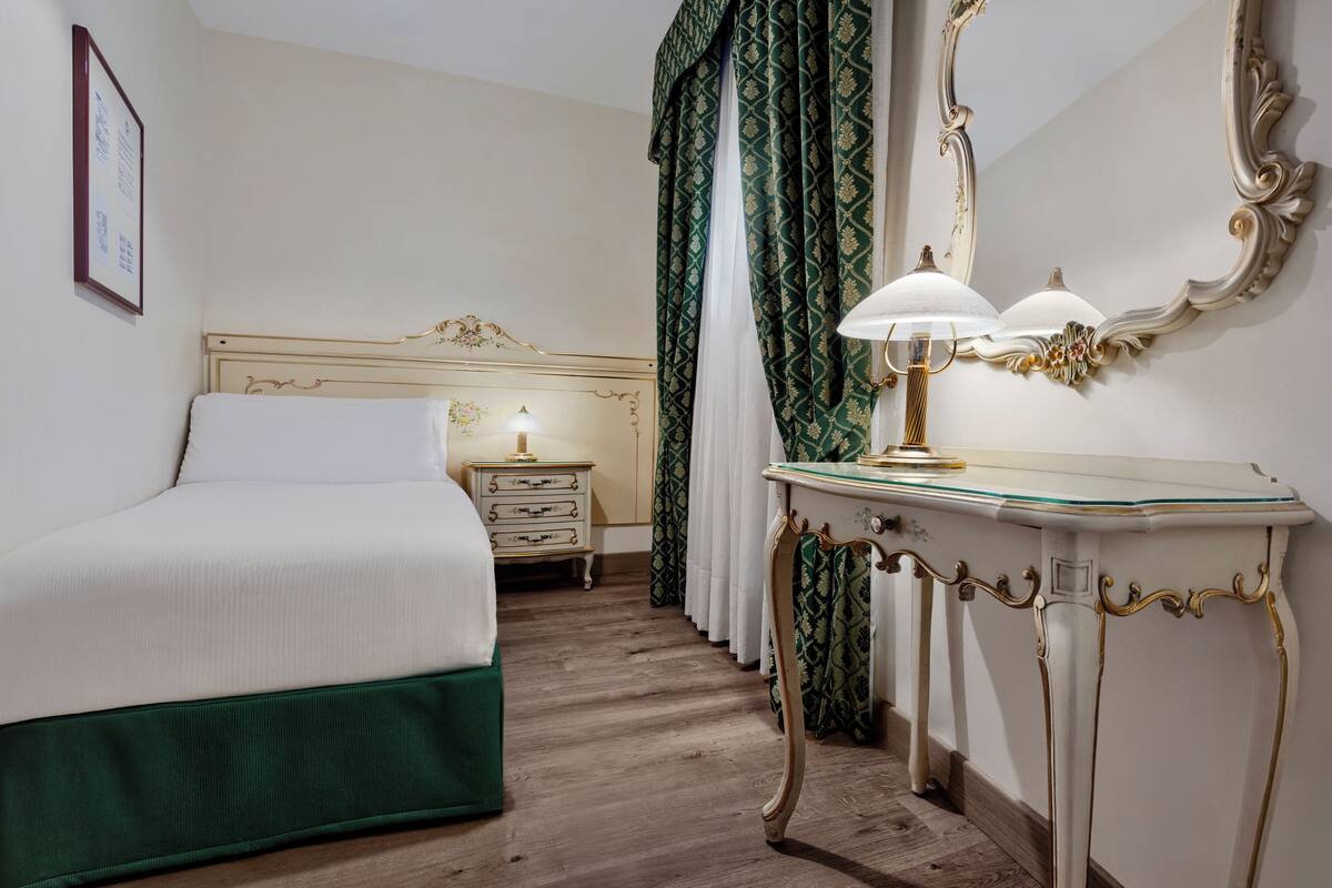 Een hotelkamer met een bed, nachtkastje, lamp, kaptafel en gordijnen.