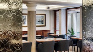 A restaurant with tables and chairs, a framed painting on the wall, and a decorative metal panel.